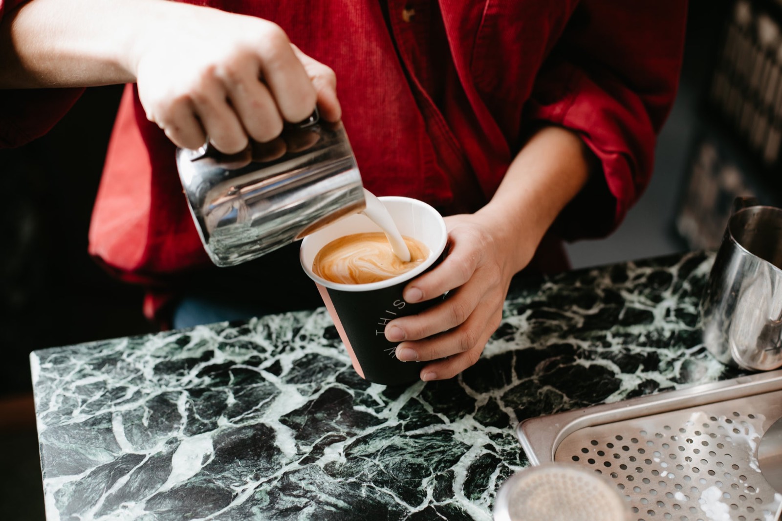 A barista pouring milk into a First Love cup